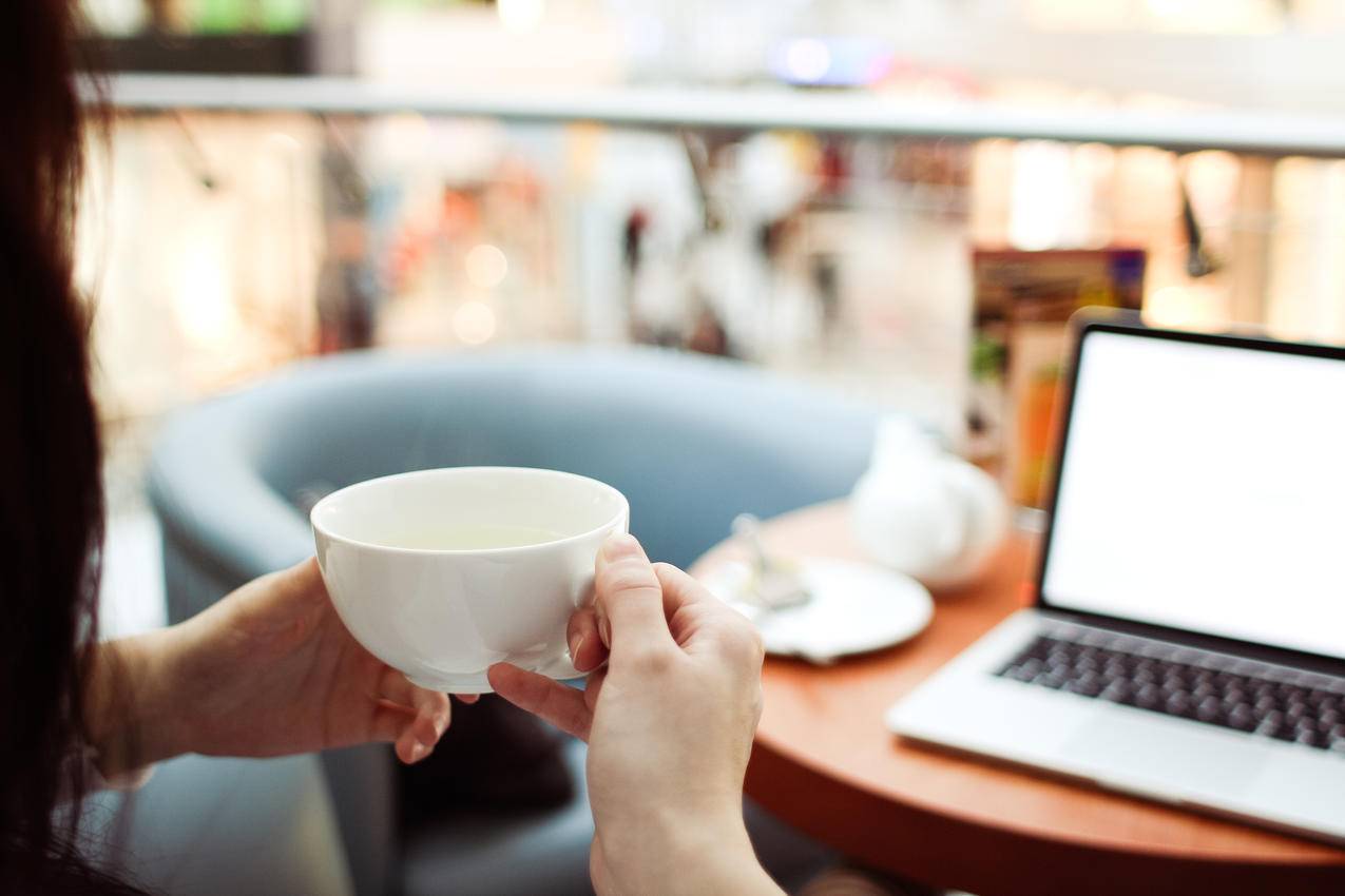 在MacBook,Pro前手持白色陶瓷茶杯的人