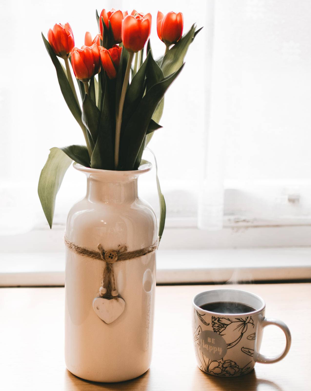 红郁金香花在白色陶瓷花瓶旁咖啡杯