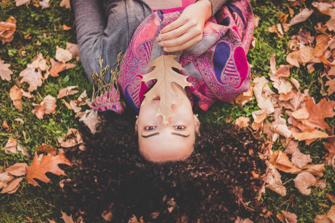 躺在绿草地上的女人抱着褐色的叶子