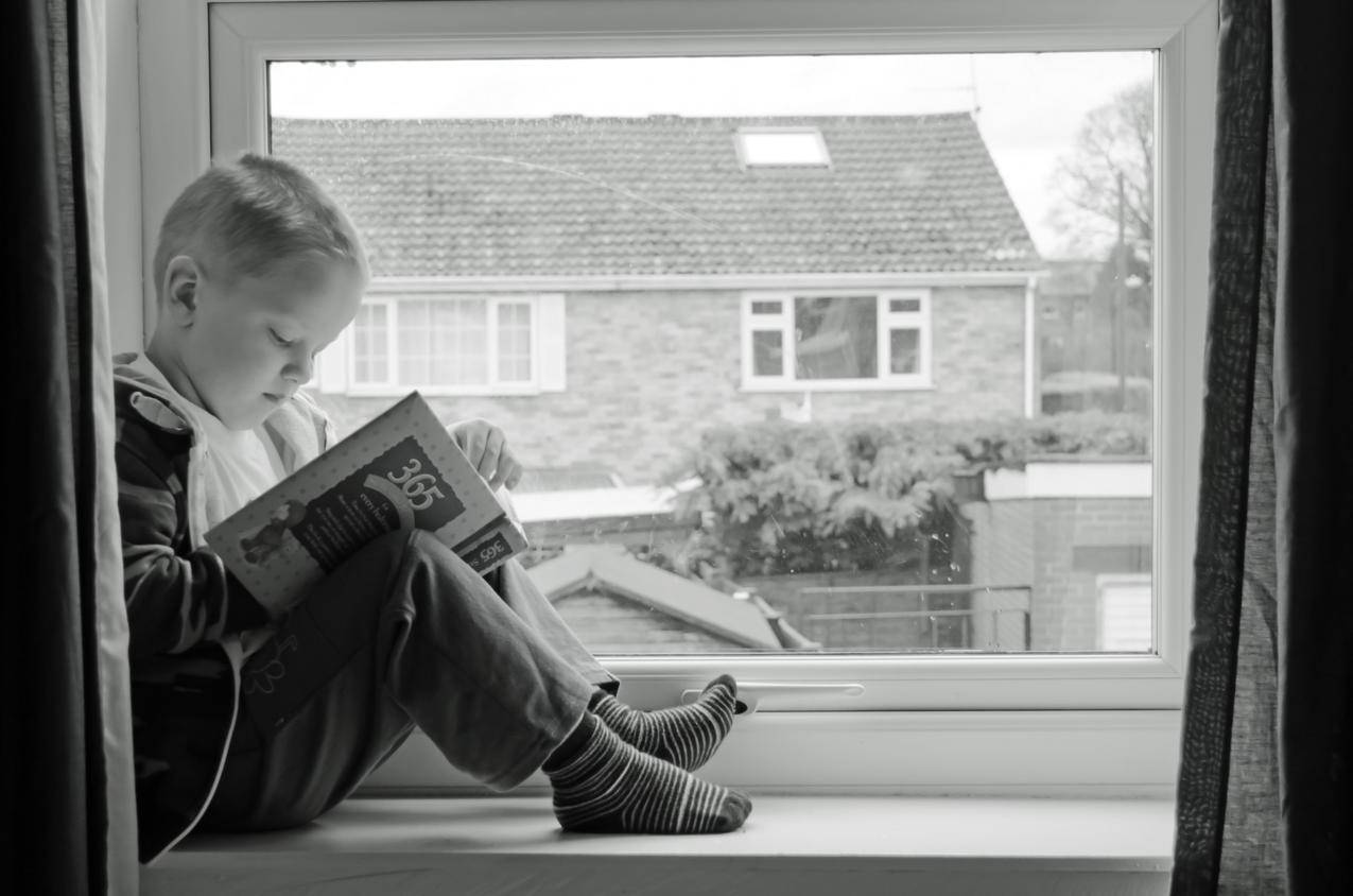 男孩在窗前阅读看书的图片