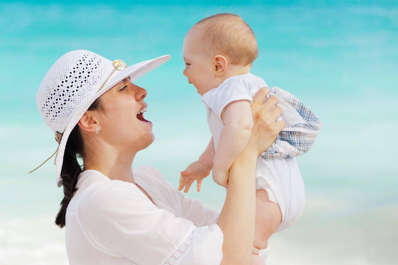 戴白帽子的妇女白天抱着孩子穿着白色的衣服靠近海滩