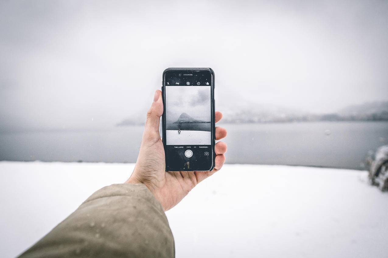 身穿棕色外套的人在拍摄山体水体时手持Android智能手机的照片