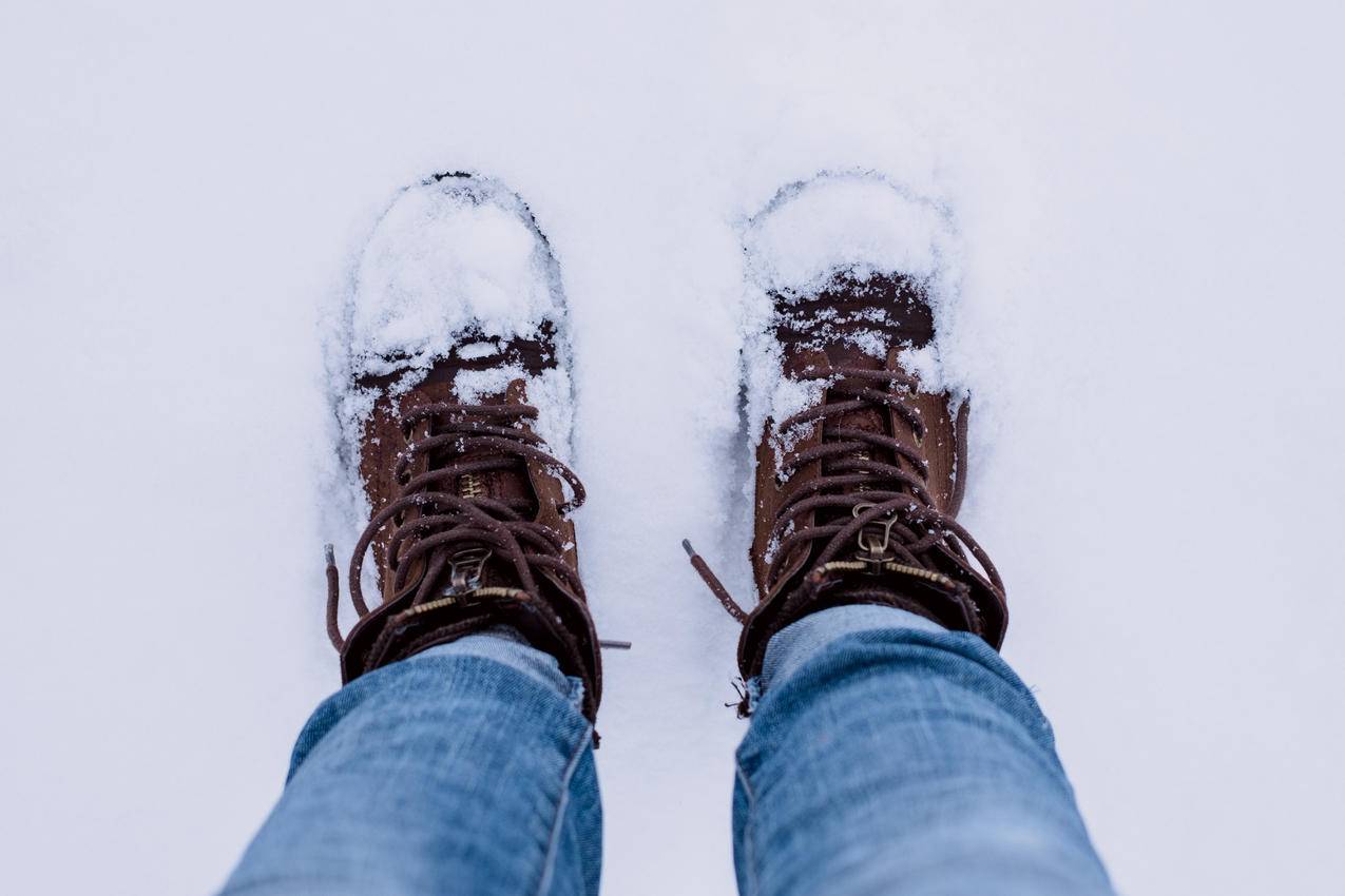 穿着棕色靴子和蓝色牛仔裤的人站在雪地上