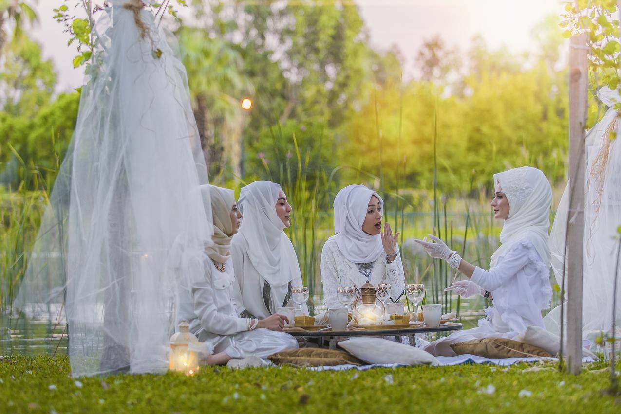4位穿着白色阿巴亚婚纱的妇女在附近野餐