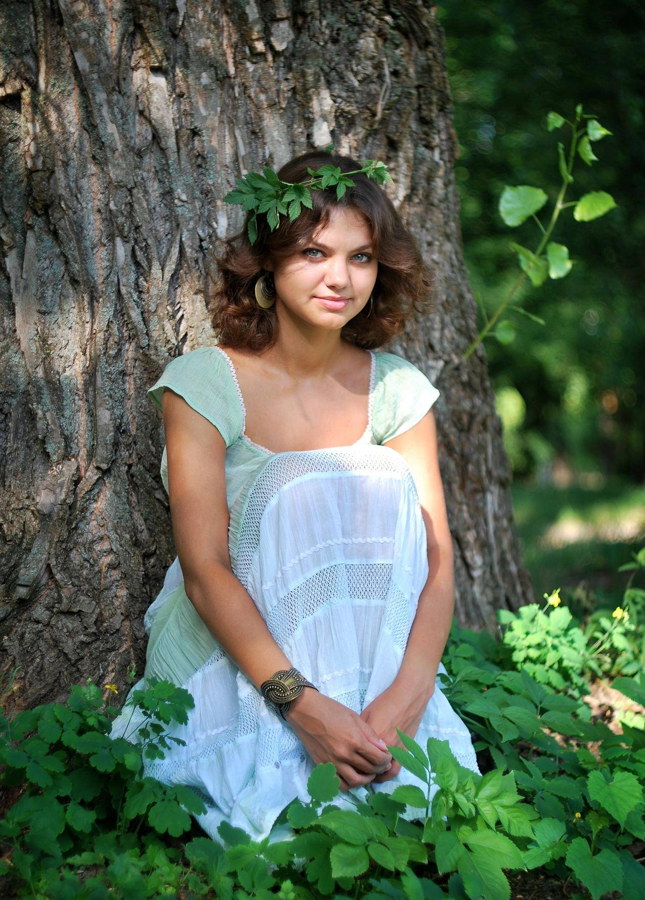 微笑着的女人穿着绿色的白叶冠,白天穿着绿色的白色无袖连衣裙坐在绿叶上