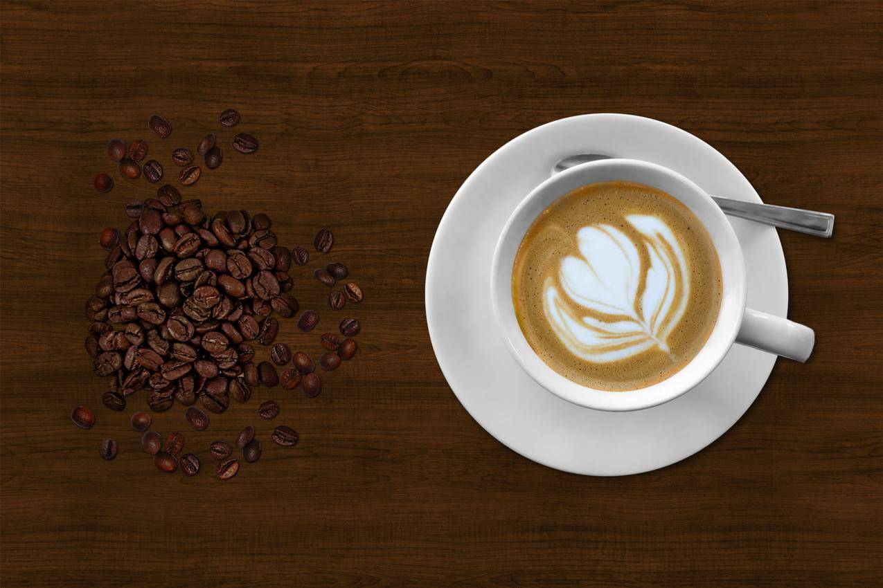 咖啡豆旁边的咖啡色咖啡杯里的棕色和白色意大利浓咖啡