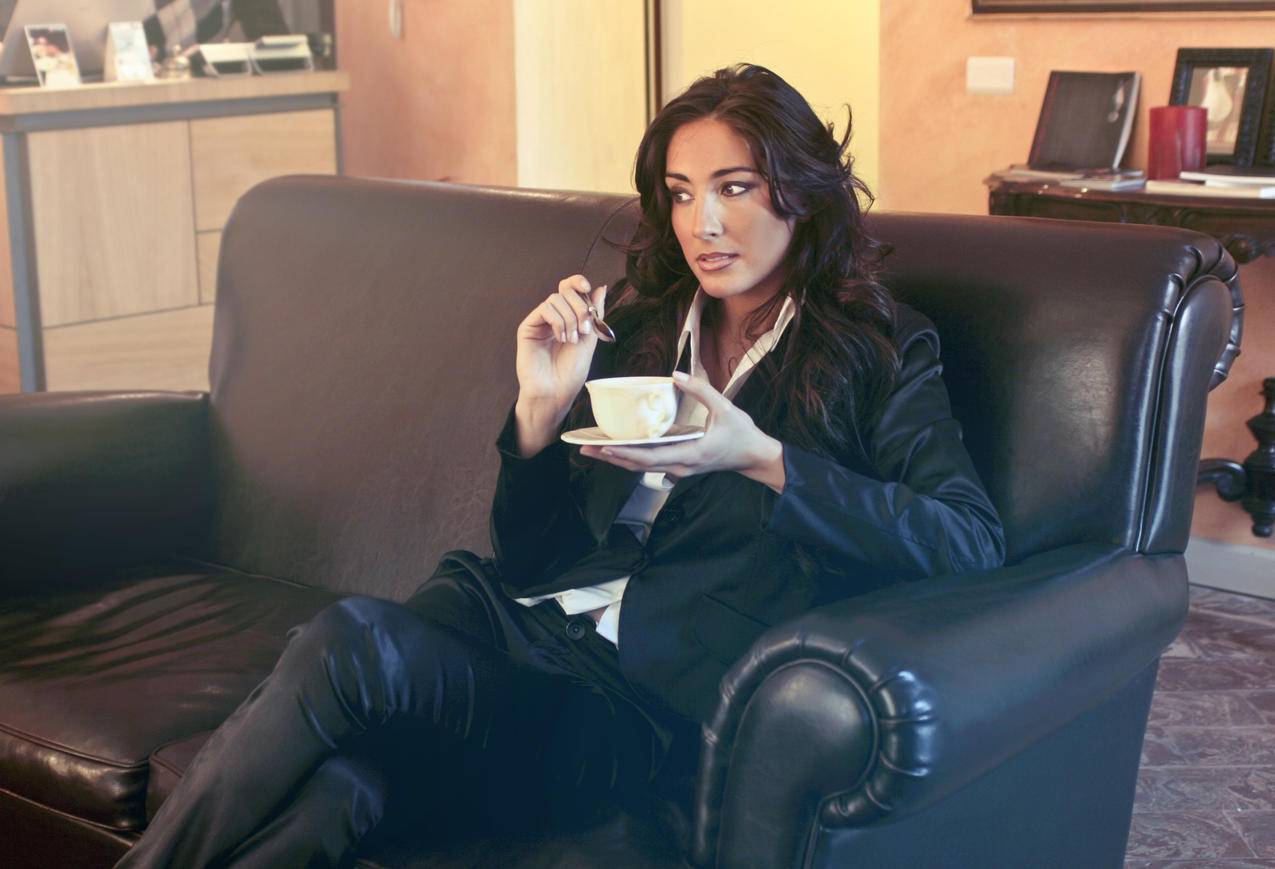 穿着黑色夹克的女人坐在黑色沙发上拿着茶杯