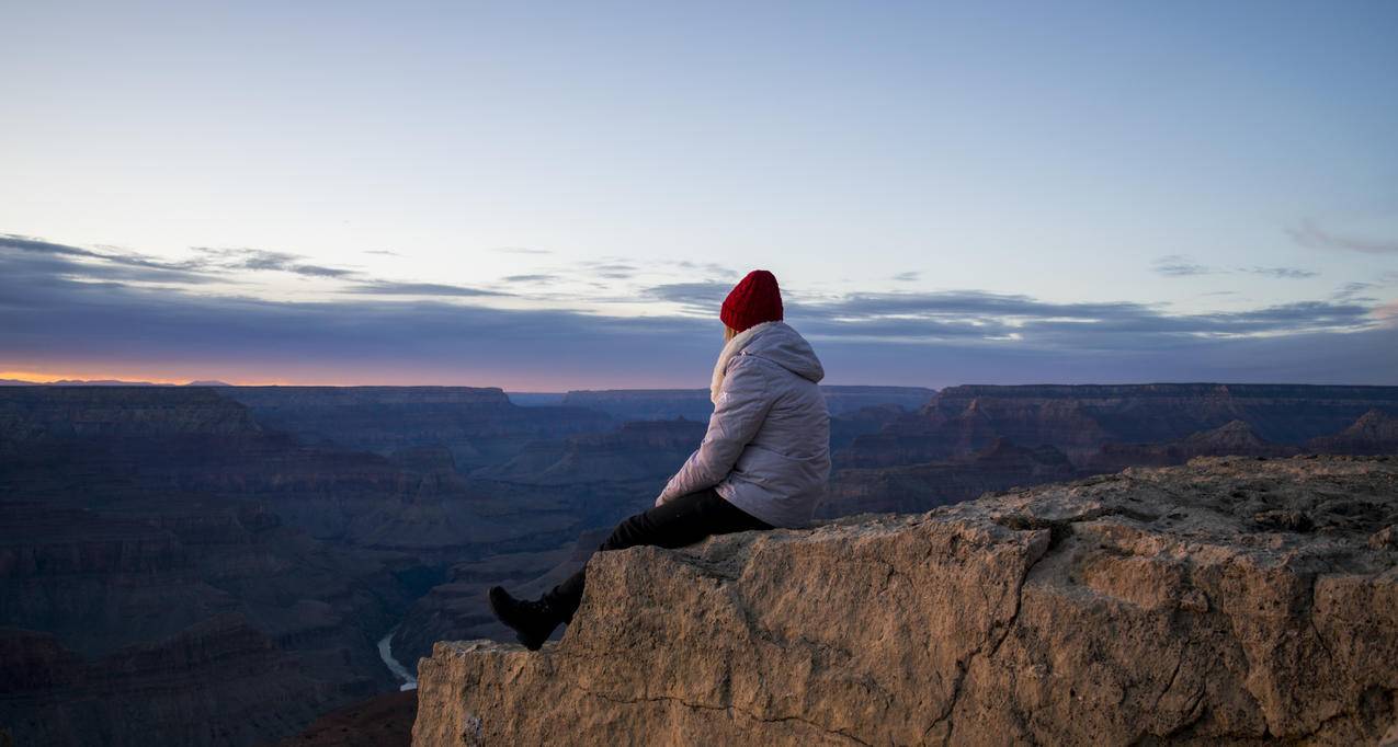 日落时穿着灰色披肩夹克和黑色短裤坐在山崖上的人
