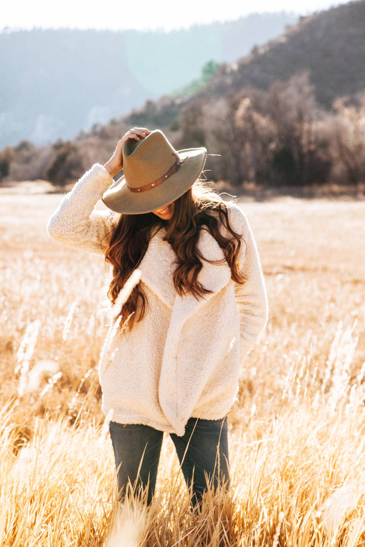 微笑的女人穿着白色的冬季夹克,棕色的牛仔帽环绕着棕色的草地