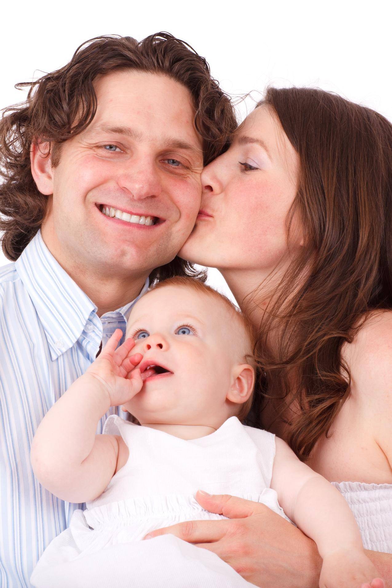 棕色头发的女人亲吻穿着白色礼服的男人穿着白色衣服的婴儿