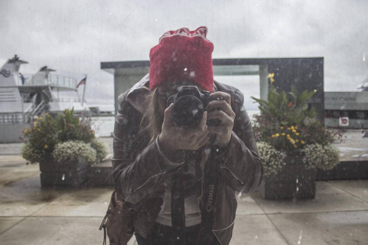 棕色皮夹克和红色针织帽的女人用黑色数码单反相机