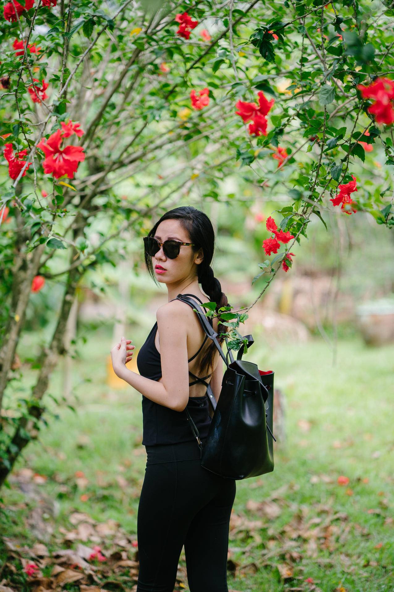 女人穿着黑色无袖上衣和黑色牛仔裤在红花芙蓉树下看她的肩膀
