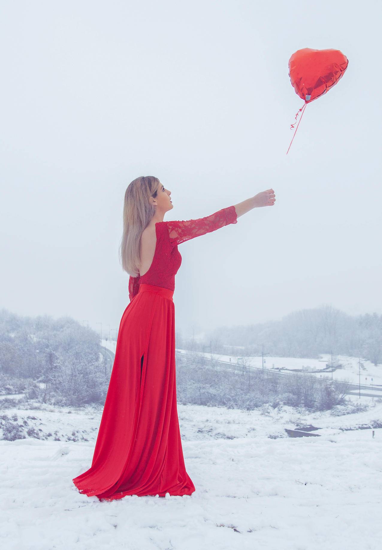 穿着红色花边长袖礼服的女士站在红心气球上