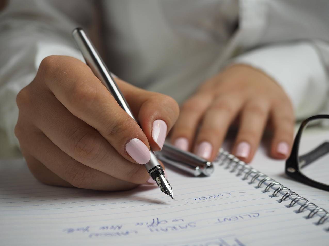 穿着白色长袖衬衫的女人拿着钢笔写在纸上