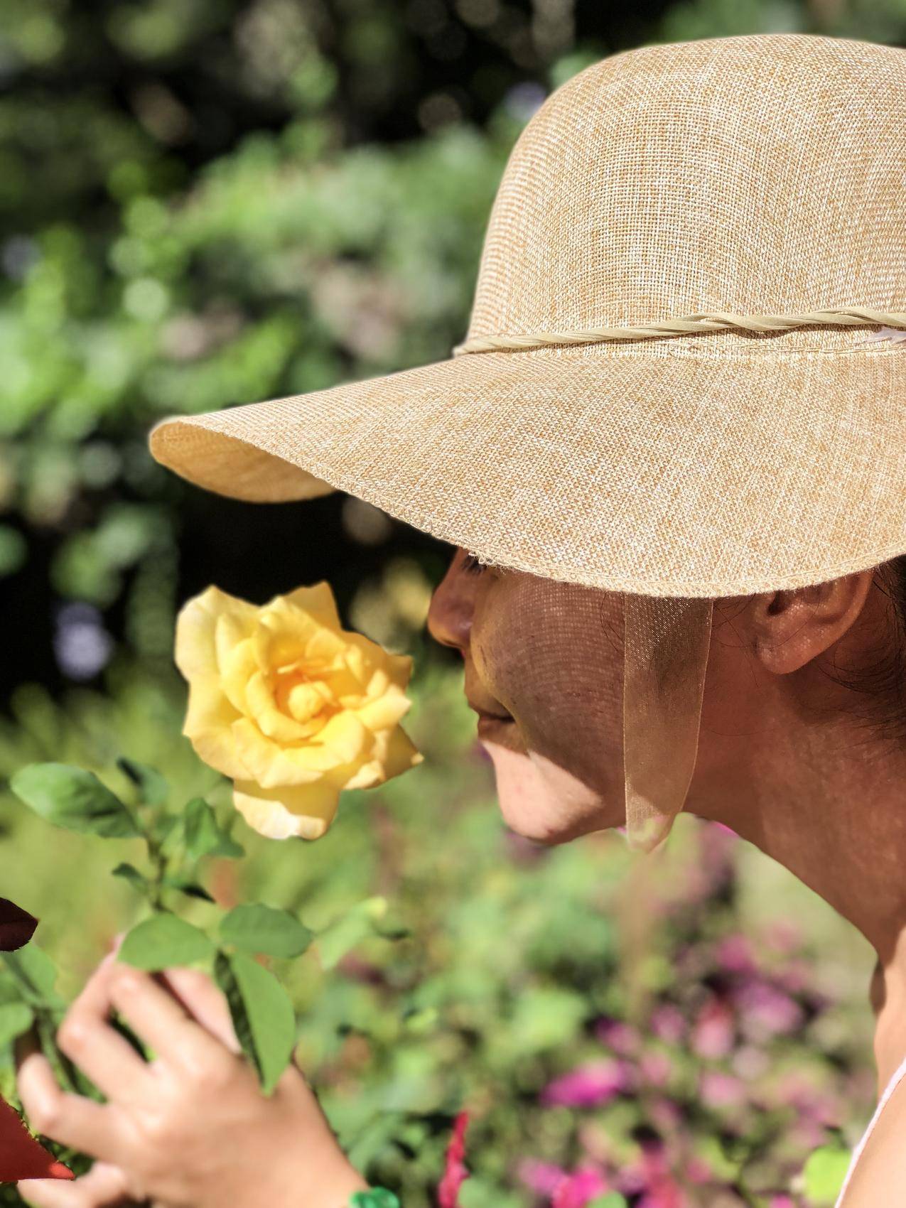 戴太阳帽闻黄色玫瑰的女人