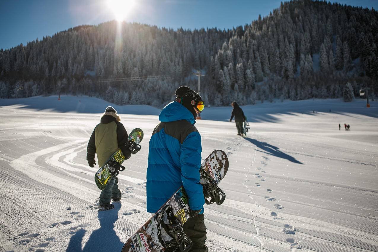 身穿蓝色冬季夹克的人在阳光明媚的天空下载着滑雪板