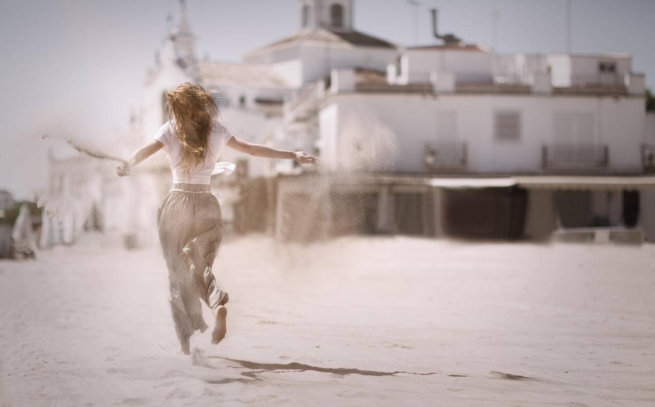 妇女在白色混凝土建筑物附近的沙丘上奔跑