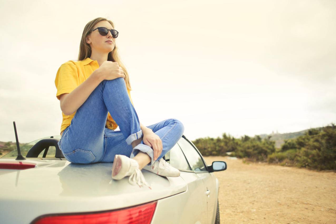 女人穿着黄色衬衫和蓝色牛仔裤牛仔裤坐在银色小汽车上