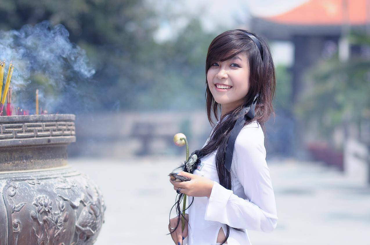 微笑的女人穿着白色长袖顶捧米色花瓣在白天摆姿势拍照