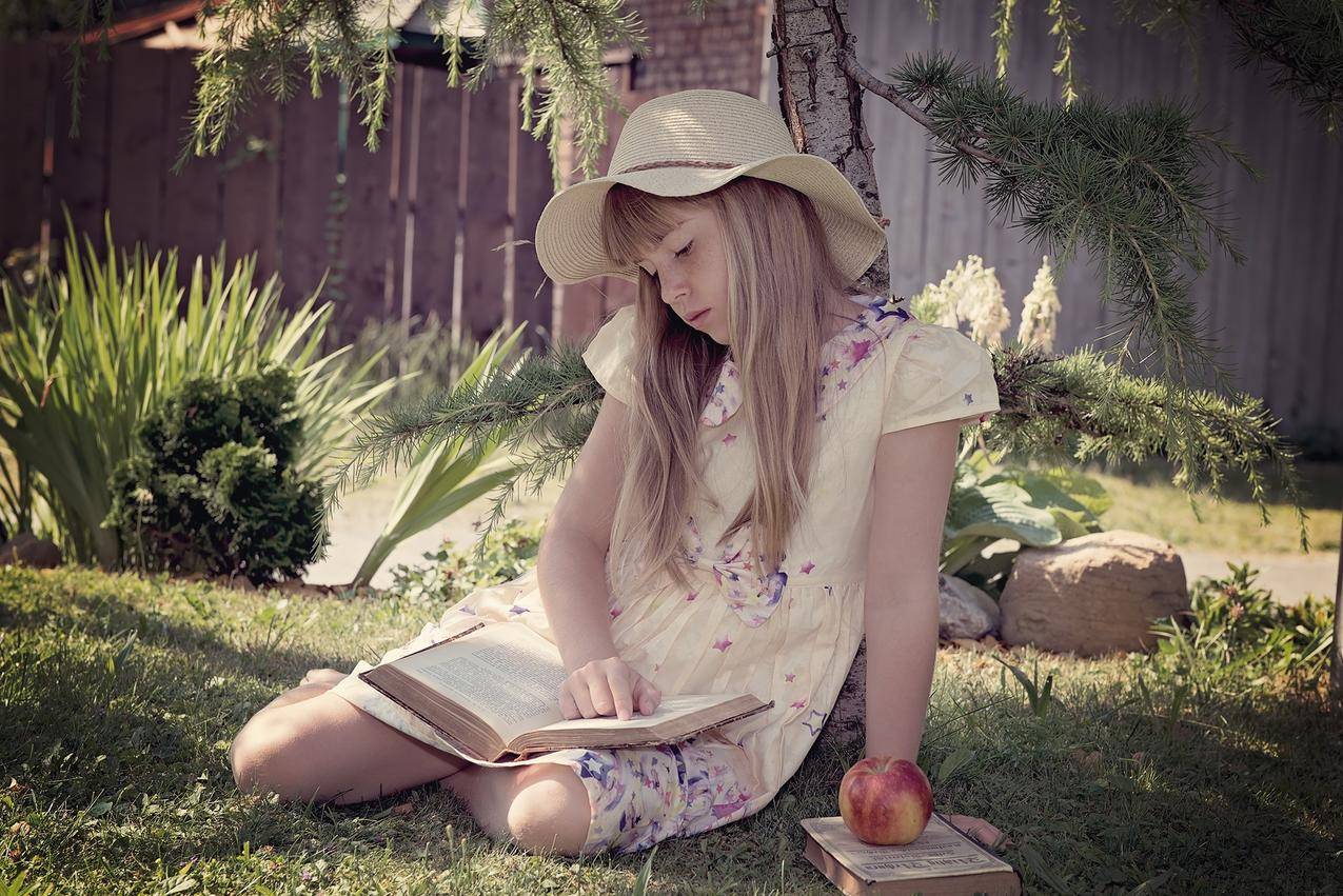 穿着白色和蓝色衣服的女孩坐在草地上看书
