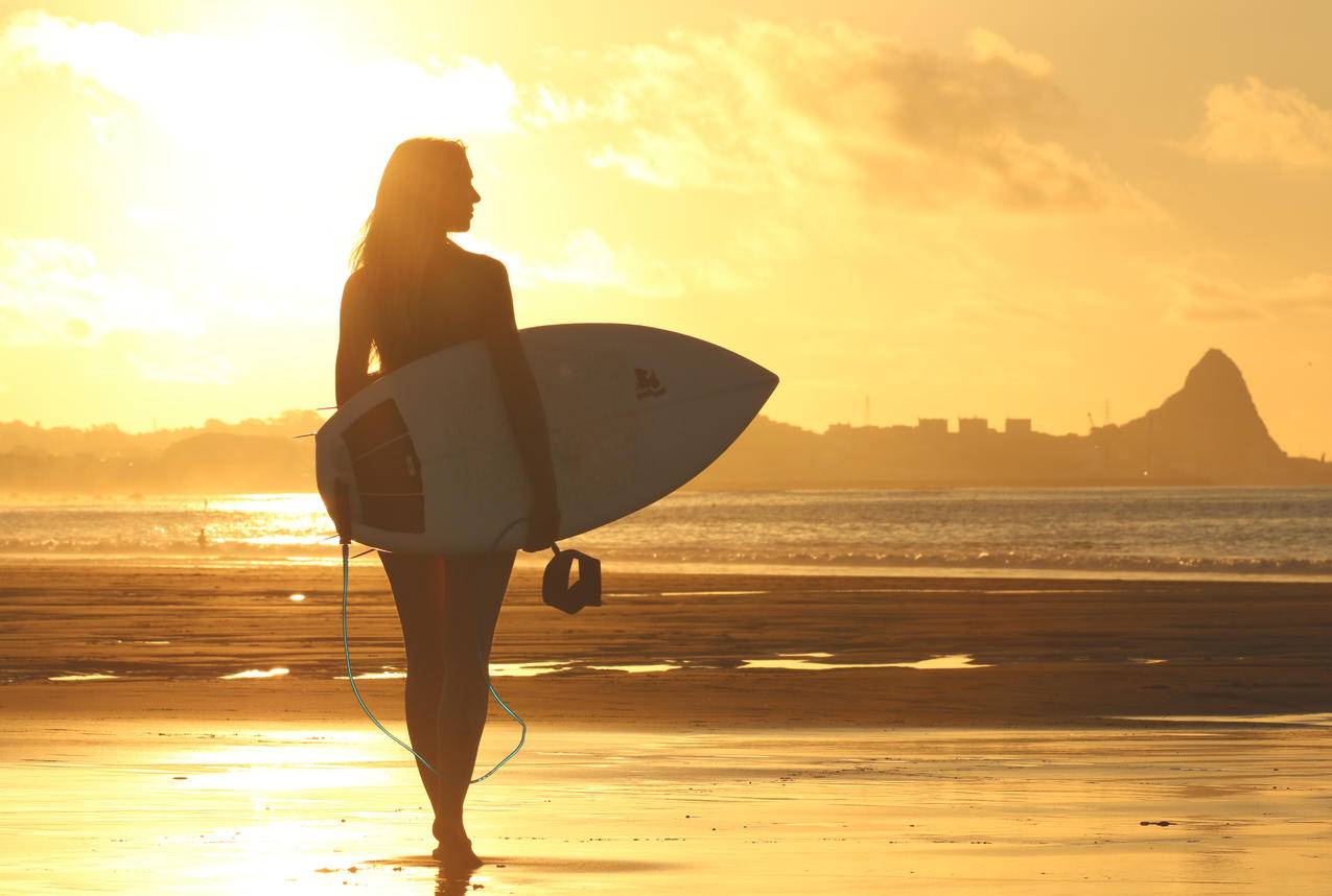 日落时站在海岸线上的冲浪板女子