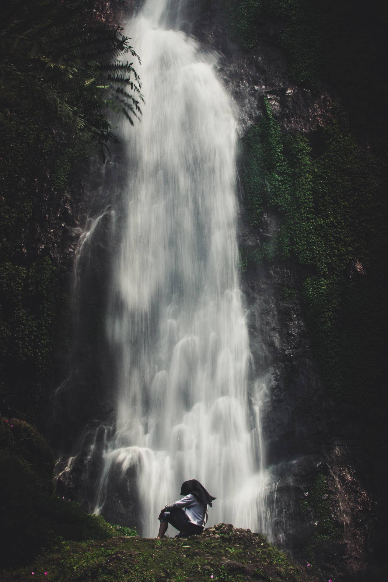 坐在瀑布附近的人的照片