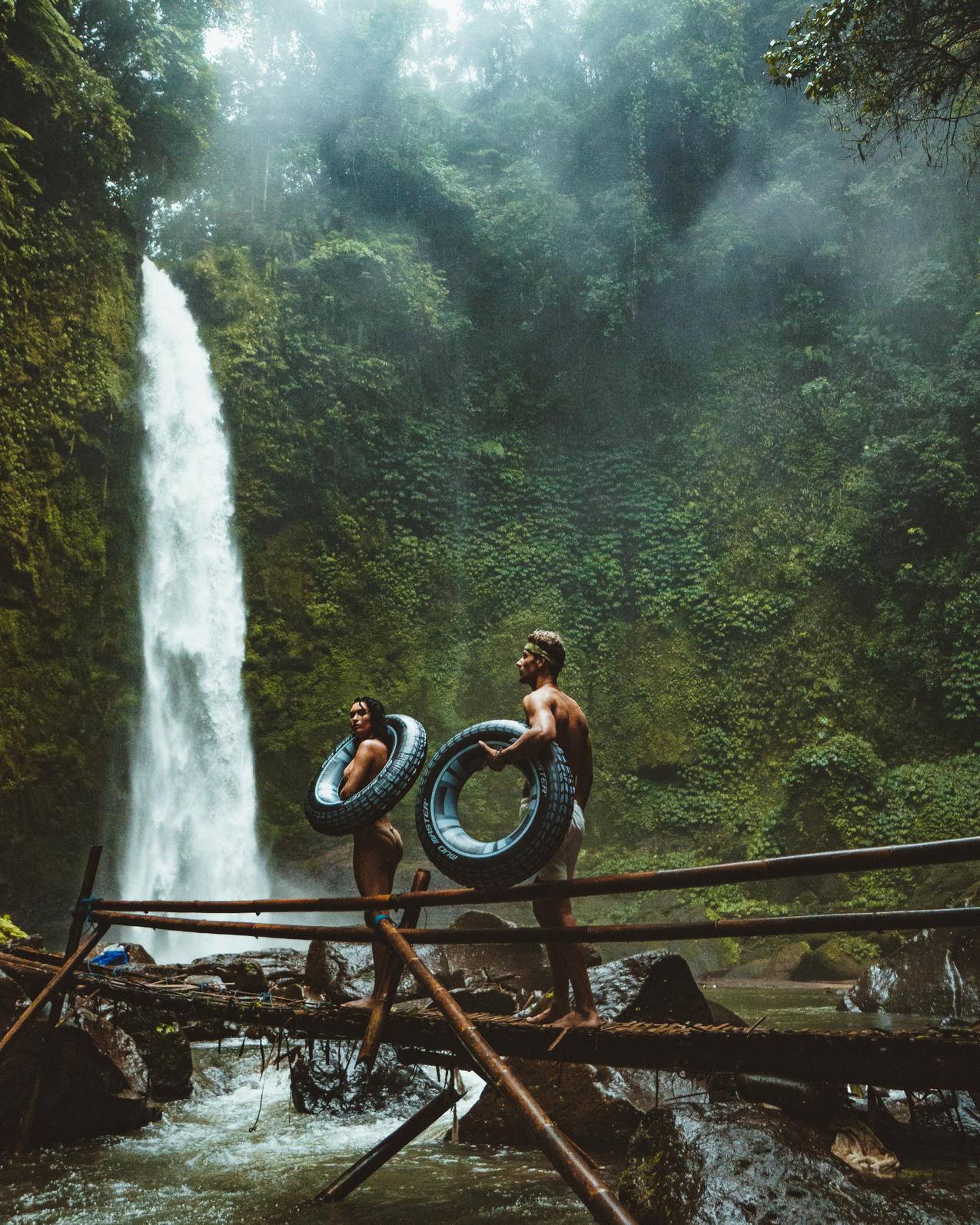 两个人携带黑色充气池漂浮在瀑布附近的棕色木桥上