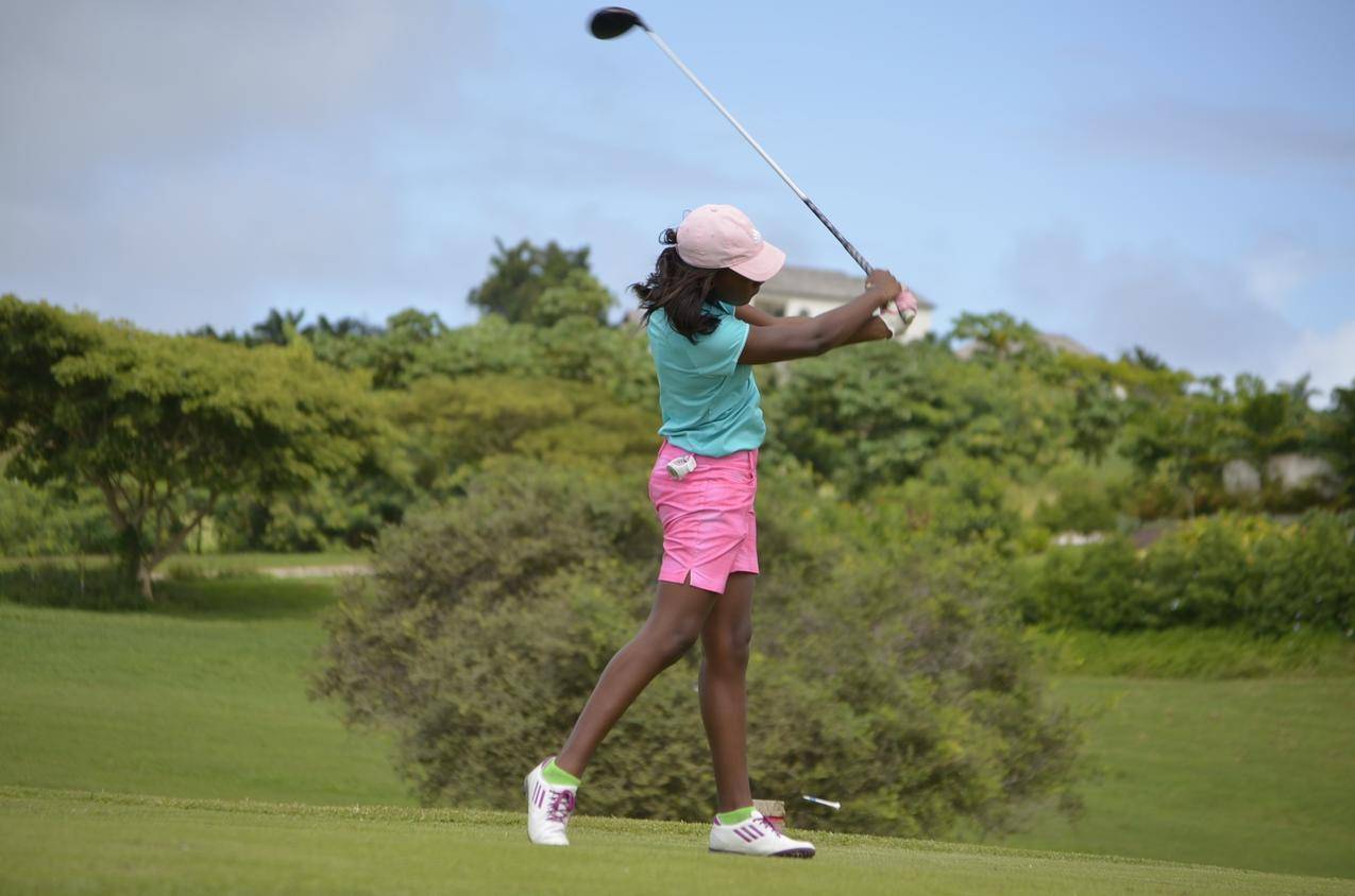 穿着绿色马球衫和粉红色短裤的女人白天在灰色和蓝色的天空下打高尔夫球