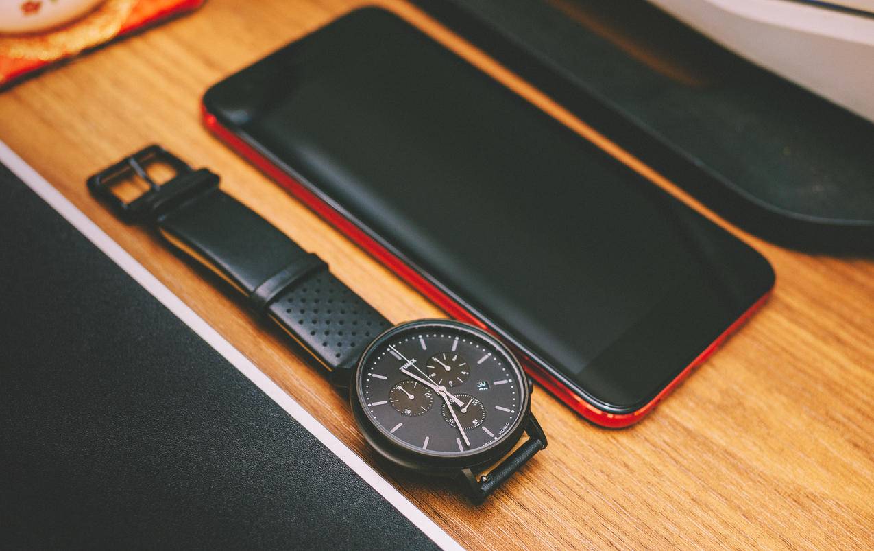 红色智能手机旁的黑色记时器看褐木板