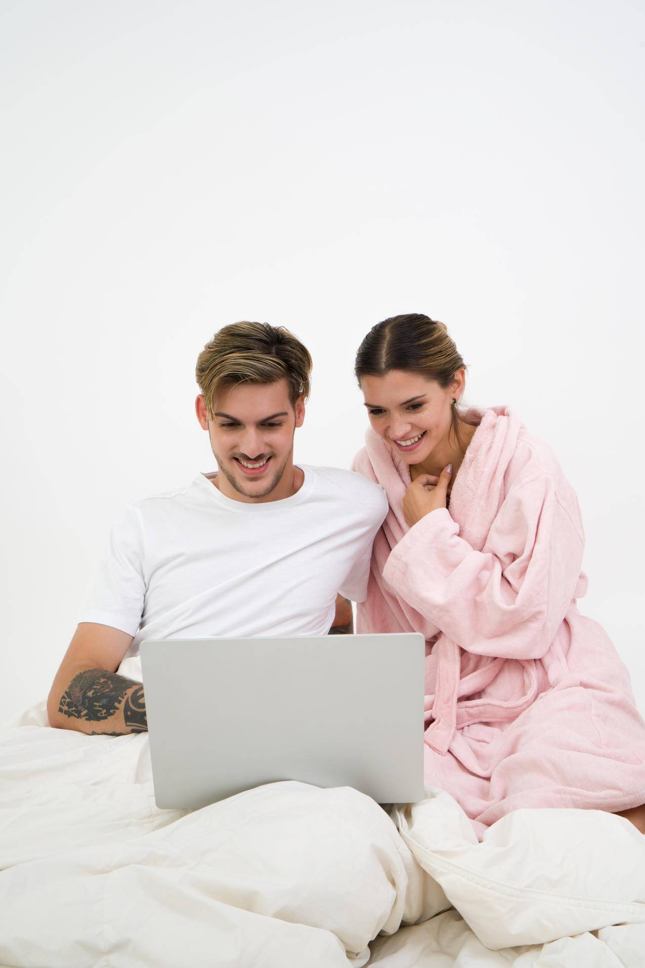 穿着白色工作服的男人坐在床旁,穿着粉红色浴衣的女人看着笔记本电脑