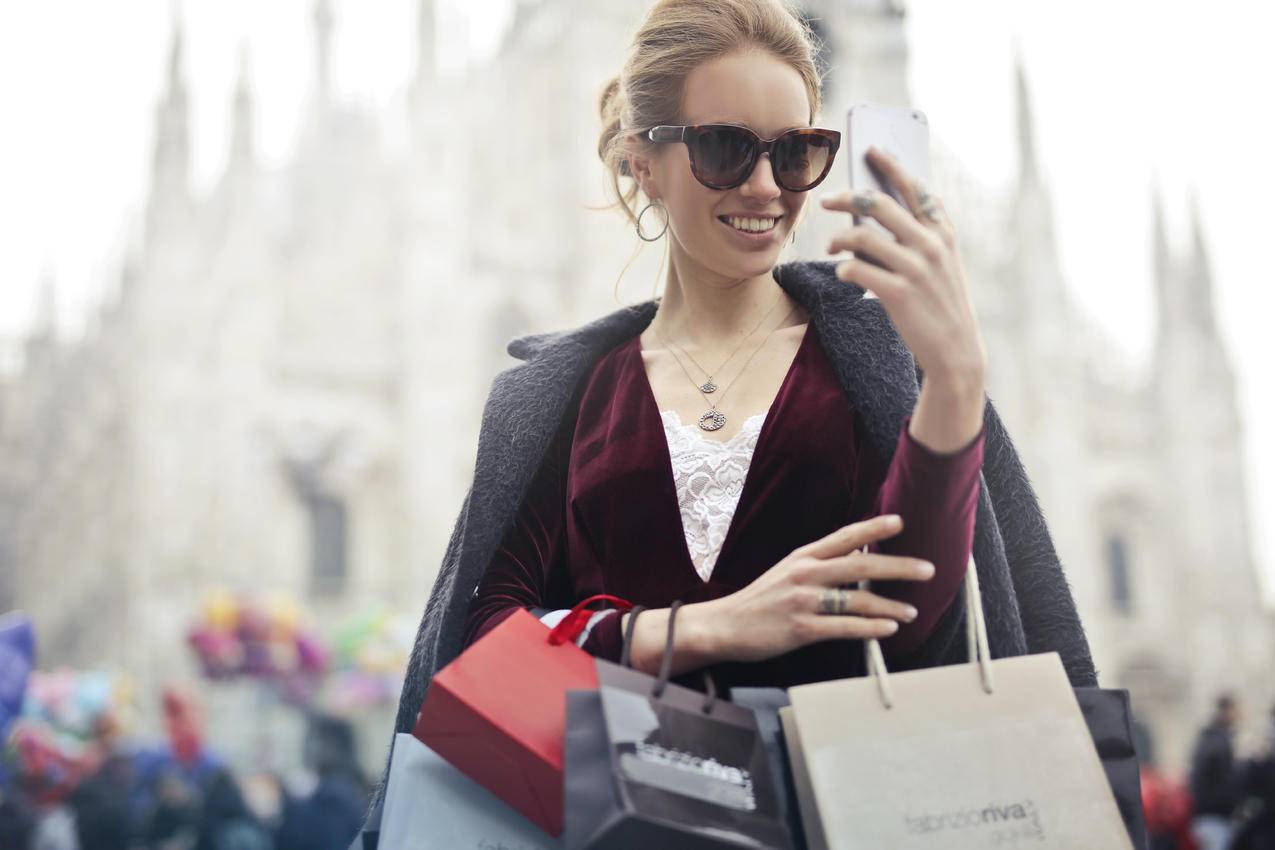 女士在栗色长袖顶部手持智能手机白天购物袋
