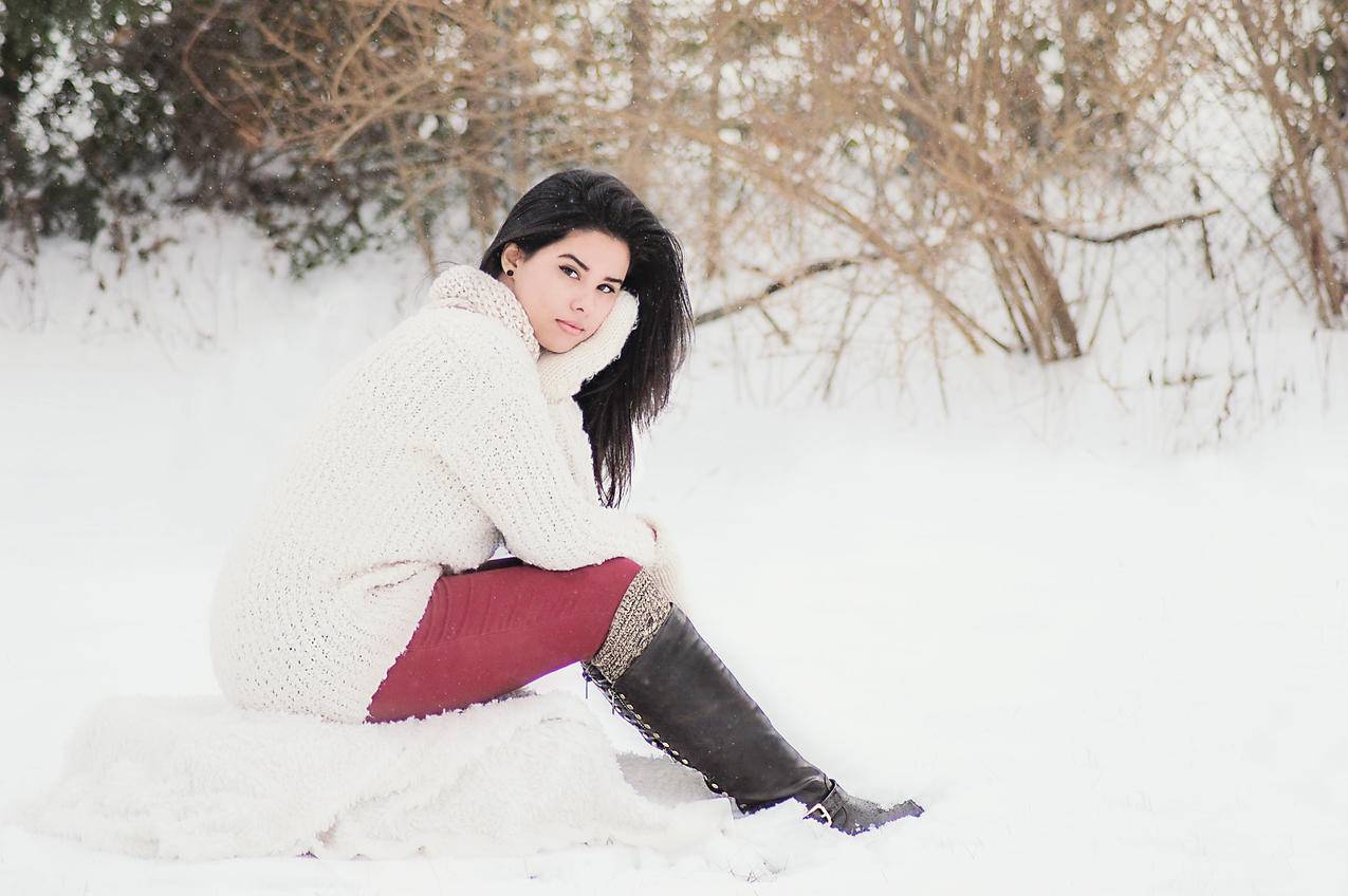 穿着白毛衣的女人在冬天坐在草地旁边