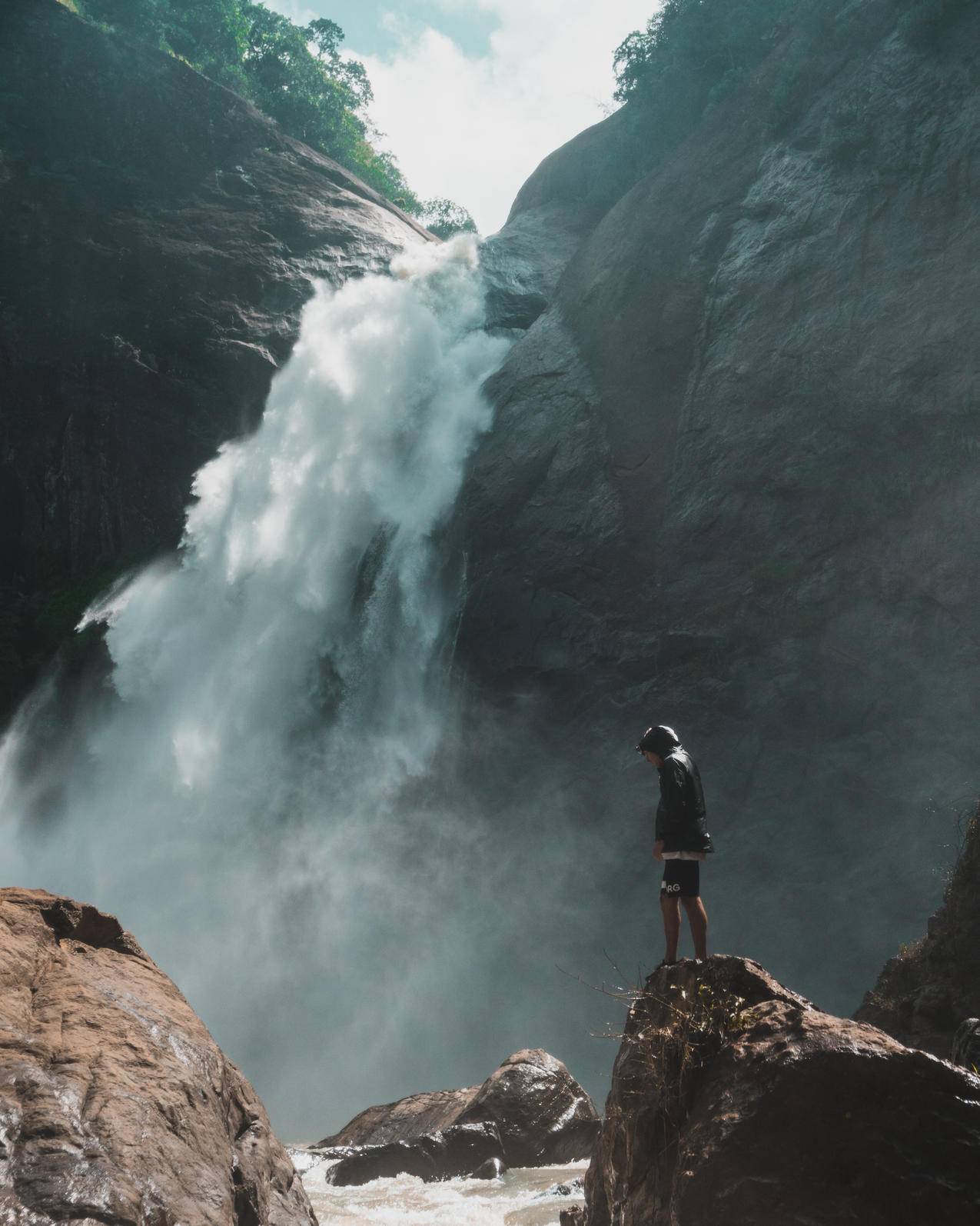站在瀑布前的棕色岩石悬崖上的人