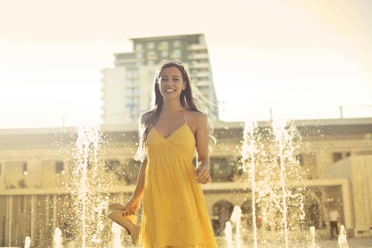 妇女穿着黄色意大利面背带裙站在喷泉旁