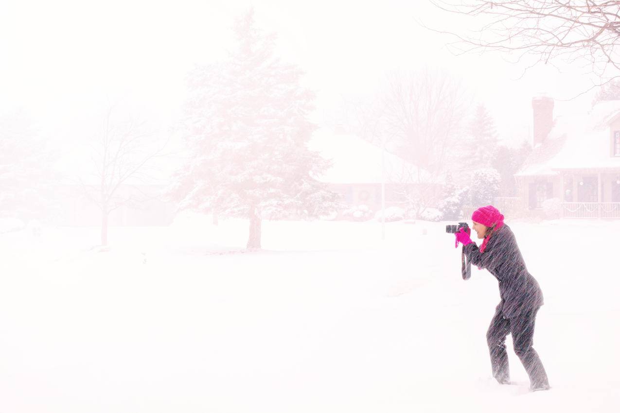 穿着粉红色数码相机的女人在白天的暴雪下手持黑色数码相机