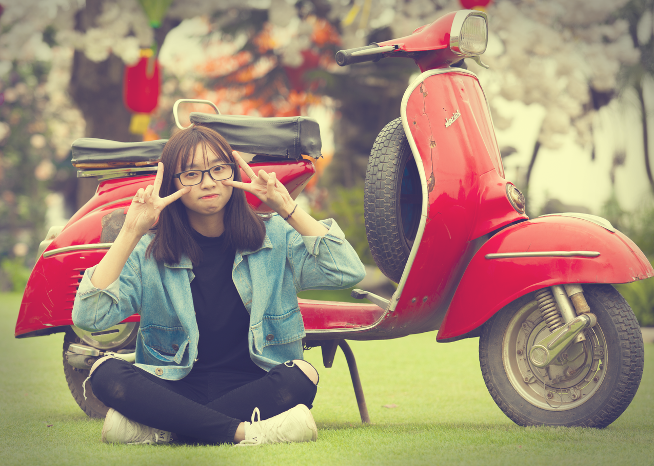 做和平手势的女孩坐在红色摩托车前