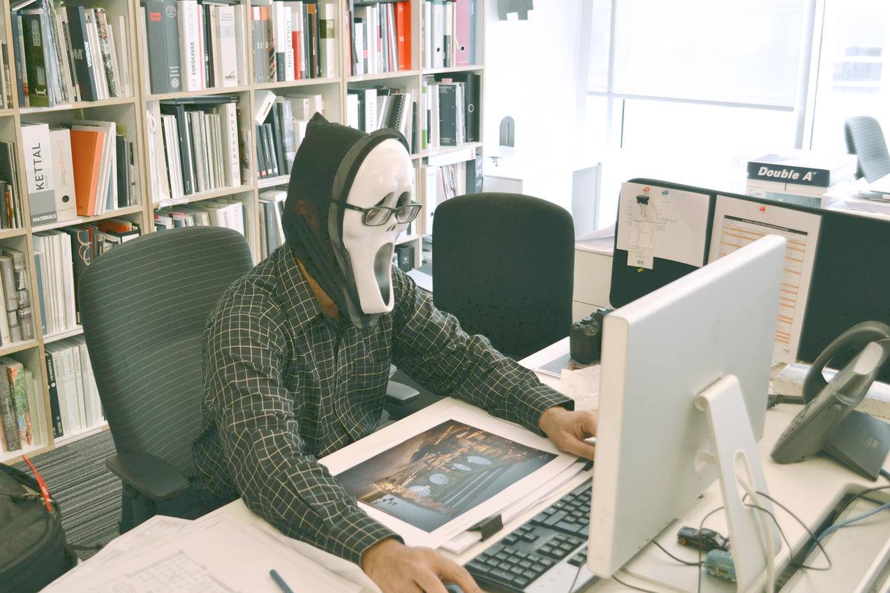 白天面对电脑桌时佩戴尖叫面具和黑色礼服衬衫的人