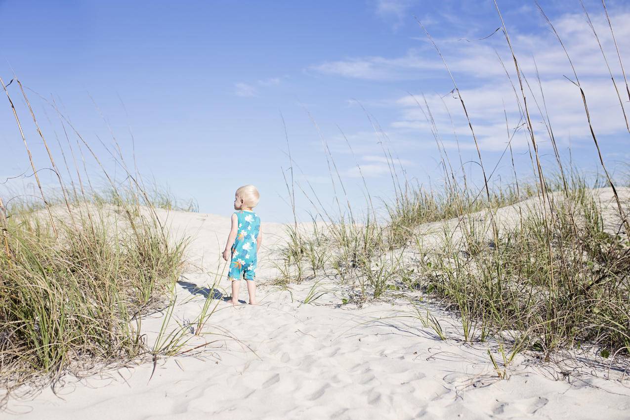 穿着蓝色衬衫蹒跚学步的蹒跚学步的孩子站在绿色草地上的白色沙滩上