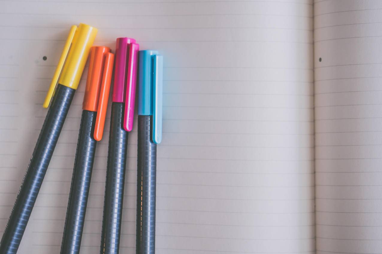 白色笔记本上的黄色,橙色,粉色和蓝色着色笔