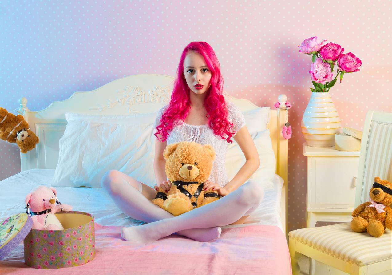 粉红长毛女人坐在双人床上,白天玩熊玩具