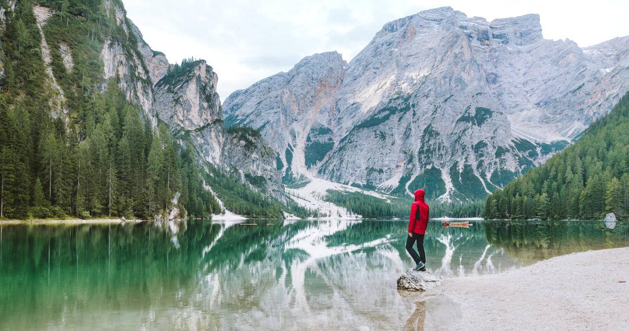 身披红色帽衫的人站在靠近山体的水域